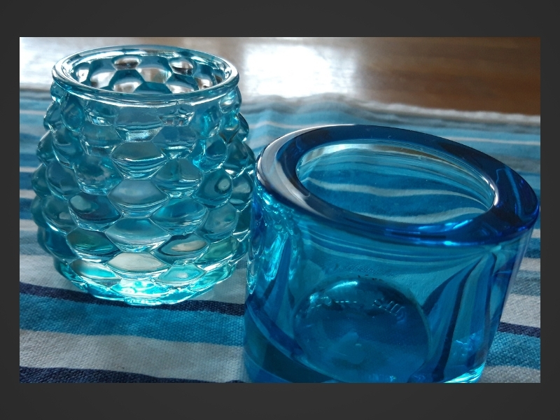 Blå-och vitrandig duk på köksbord av ek, två blå värmeljuslyktor i glas.